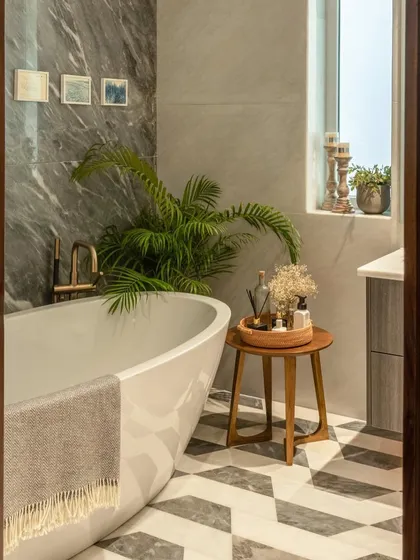 A freestanding tub is the ultimate luxury. Here, it's placed against a grey marble accent wall, with patterned flooring and lush greenery creating a serene, spa-like environment at home.