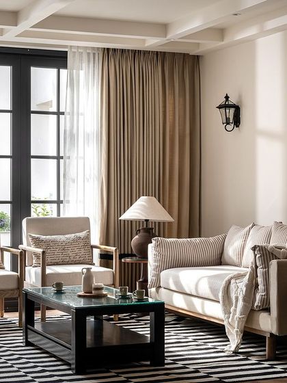 This living space from Riviera Maison is inspired by French colonial design. We used a palette of beige and black, with natural wood armchairs and a striped rug to create a look that is both classic and relaxed.