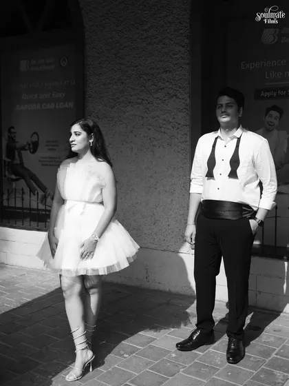A full-length black and white portrait with a classic, almost stoic feel. The strong shadows and their formal attire give this image a timeless, sophisticated, and slightly mysterious quality.