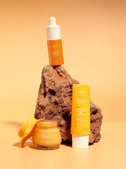 A product family shot for a Vitamin C skincare range. The products are styled on a rock against a warm, sandy-colored background, giving the line an earthy and natural feel.