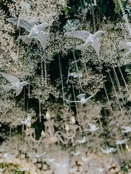 Detail of the ceiling treatment for the elegant white engagement party. A canopy of baby's breath is interspersed with hanging crystal birds and delicate chandeliers, adding layers of texture and enchantment to the overall design.