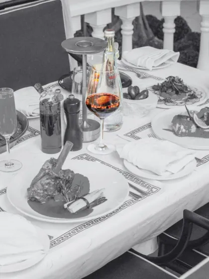 A perfect meal is complemented by the perfect wine. This artistic shot captures a glass of rich red wine, the centerpiece of a table laden with our finest dishes, ready for an evening of indulgence.
