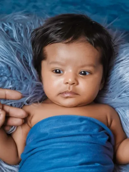 A wide eyed newborn holds onto his parents' fingers, nestled in a soft blue wrap. We capture these early moments of connection and curiosity.
