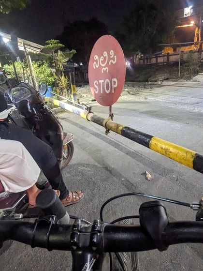 A point-of-view shot from the handlebar, waiting at a closed railway gate. It's a moment of pause, a chance to soak in the unique atmosphere of the city at night.
