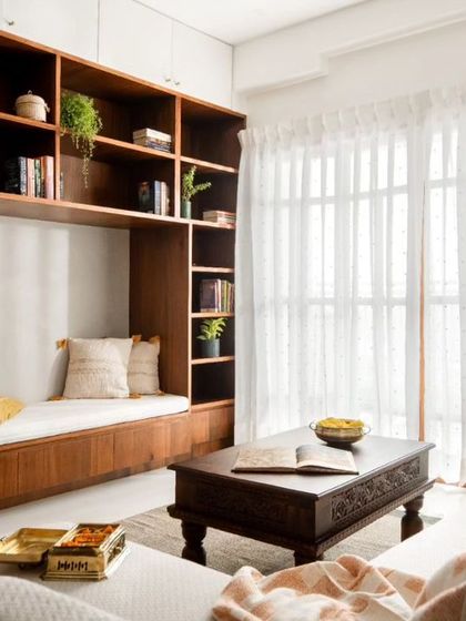 The custom-built reading nook is integrated into a large bookshelf, creating a perfect spot for relaxation. Sheer curtains diffuse natural light, making the space bright and airy.