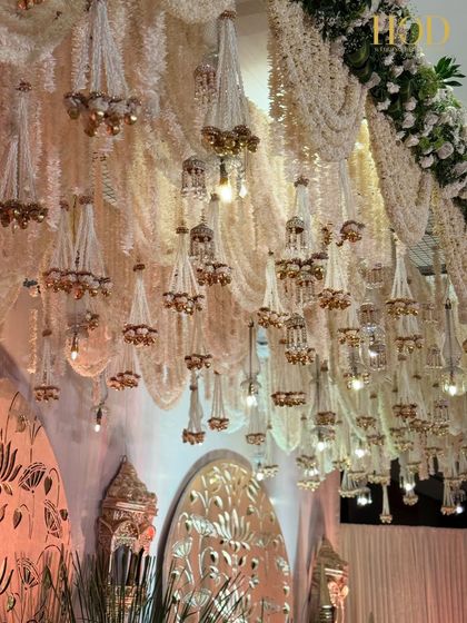 A breathtaking ceiling installation of hanging floral chandeliers made of white flowers and golden bells, creating a sense of opulence and grandeur.