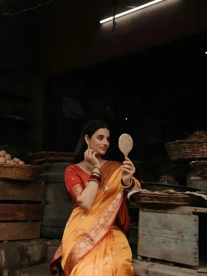 A classic portrait of a woman in a saree, holding a mirror, set against the moody, dark backdrop of a traditional Indian market.