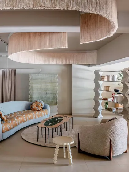 This lounge setting within the JOSMO store showcases a curated collection of furniture. A flowing fringe installation overhead defines the space, while the mix of a patterned sofa and textured armchairs creates an eclectic and inviting atmosphere.