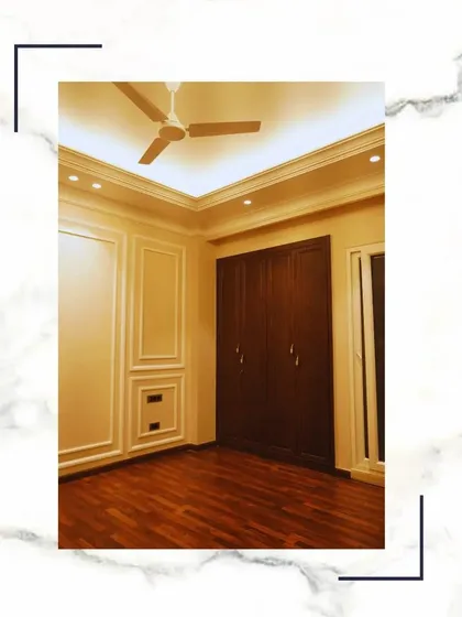 A bedroom featuring rich wooden flooring and a matching built-in wardrobe. The classic wall paneling and simple false ceiling create a cohesive and elegant look.