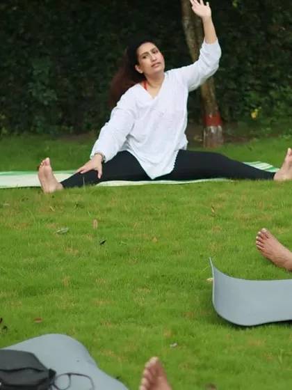 Guiding a group through gentle stretches on a lush green lawn. My outdoor yoga classes are designed to be accessible for everyone, focusing on feeling good in your body.