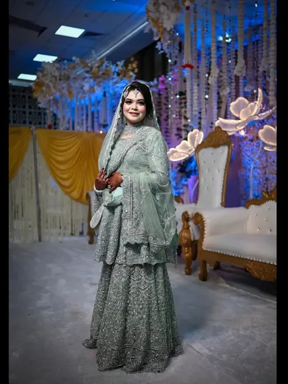A full-length portrait of the bride at her reception, showcasing her stunning lehenga against the beautifully decorated stage. She looks every bit the elegant bride.