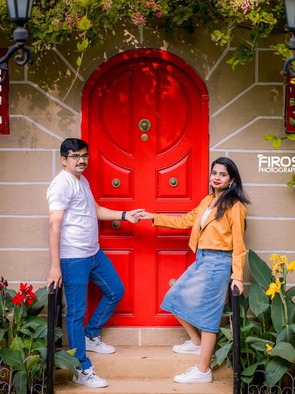 A couple poses by a bright red door, part of our colorful and charming European-inspired sets.