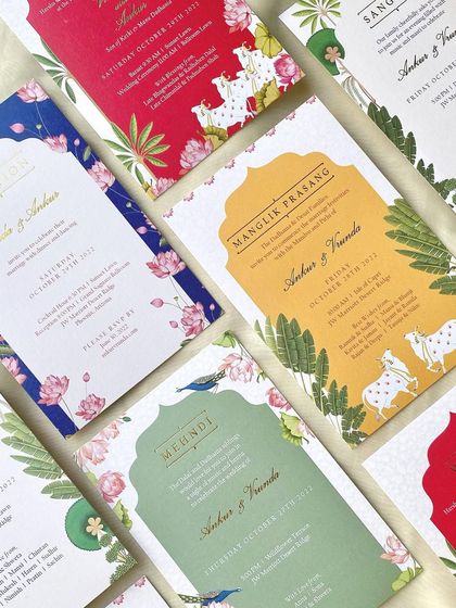 A vibrant collection of invitation cards for a wedding in Phoenix, Arizona. Each card uses a different bright color and custom illustrations, including pichhwai-style cows and tropical florals, to represent the various ceremonies.