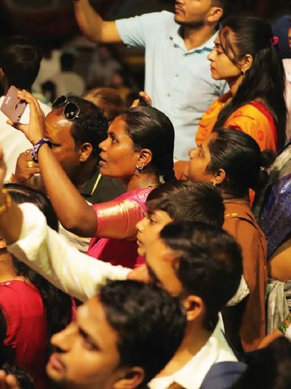 A crowd of people in Varanasi, phones held high, capturing the spectacle above. The collective experience of watching a story unfold in the sky brings communities together.