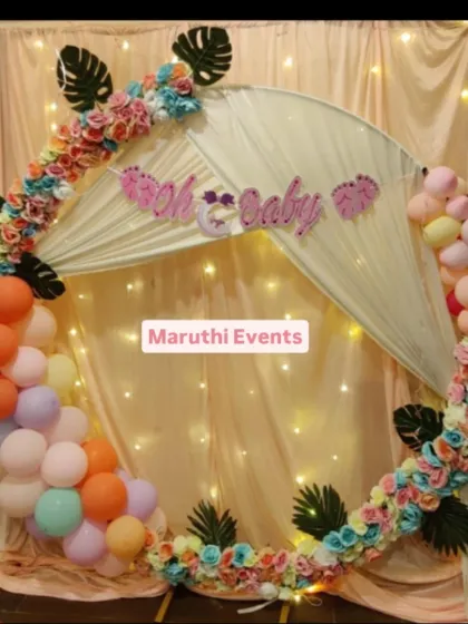 A lovely "Oh Baby" shower with a floral and balloon ring. The pastel-colored balloons are mixed with paper flowers and monstera leaves, with fairy lights adding a warm glow.