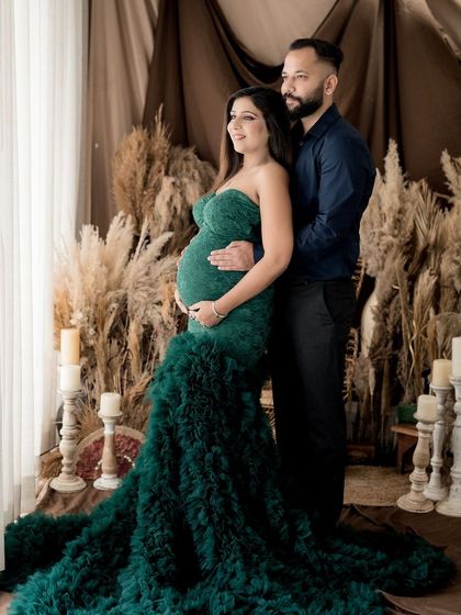 A classic pose for a couple's maternity shoot, with the rich green gown creating a stunning contrast against the neutral, earthy tones of the backdrop.