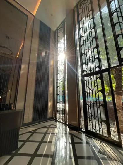 Sunlight streams through the tall, ornate window screens of a residential lobby in Mumbai. This design element not only adds security and privacy but also creates beautiful, shifting patterns of light within the entrance space.