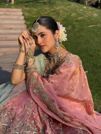 A beautiful seated portrait. The styling showcases the intricate hand jewelry and the beautiful floral arrangement in the hair, completing this traditional pastel look.