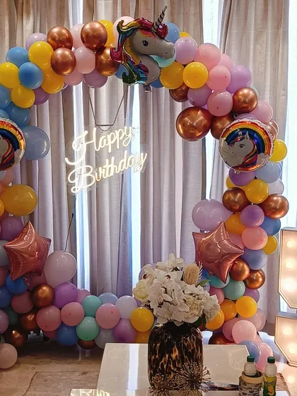 A unicorn and rainbow themed birthday party. This setup features a large circular balloon arch, a 'Happy Birthday' neon sign, a light-up number '5', and unicorn foil balloons.