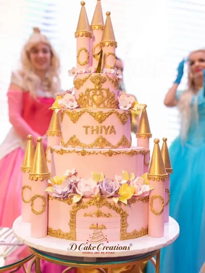 A grand princess castle cake for Thiya's first birthday, with real-life princesses in the background. This multi-tiered pink and gold cake is the definition of a royal celebration.