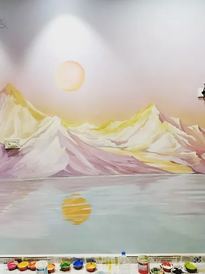 Another view of the mountain lake mural, showing the reflection of the sun on the water. The paints are still visible at the bottom, offering a behind-the-scenes look at the creation process.