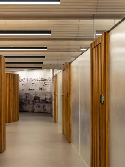 A hallway in the updated UTI HQ features curving, slatted wood partitions that create a rhythmic, sculptural effect while housing private offices.
