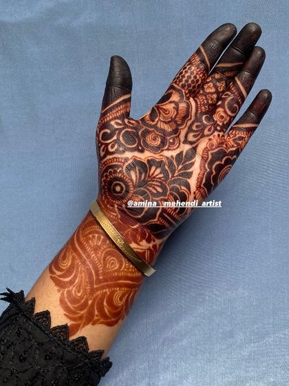 The dark, almost black stain on the fingertips contrasts beautifully with the reddish-brown floral patterns on the wrist.