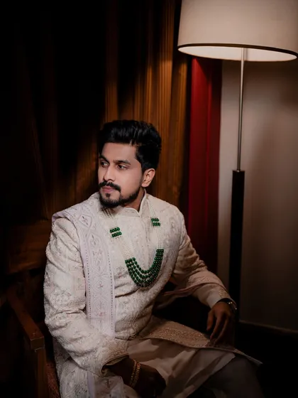 A handsome, seated portrait of the groom in his wedding sherwani, looking thoughtful and composed before the ceremony.