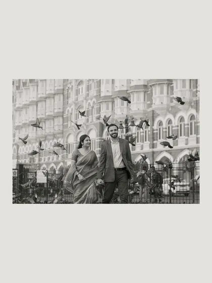 A beautiful black and white shot of the couple walking past the Taj Mahal Palace hotel, with pigeons taking flight around them, creating a classic and romantic scene.