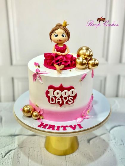 A special cake to celebrate 1000 days of a little princess. This pink and white cake is decorated with gold spheres and a custom fondant doll wearing a crown.