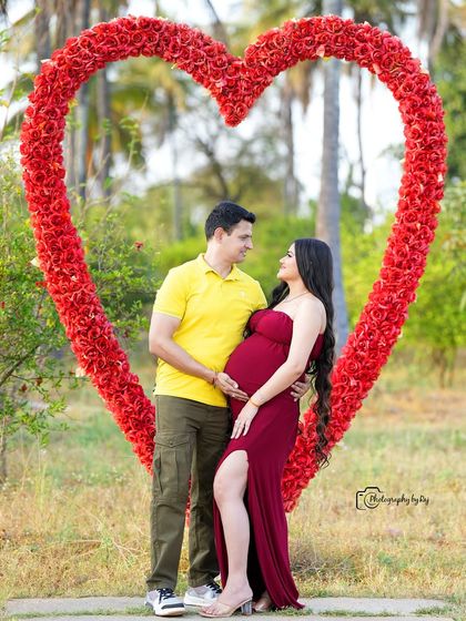 A romantic couple's portrait framed by our red floral heart prop. The mother-to-be is wearing a simple red dress.