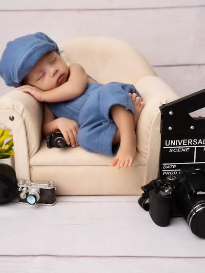 A future director in the making. This creative newborn theme features a sleeping baby on a mini sofa, surrounded by camera equipment and a movie clapperboard.