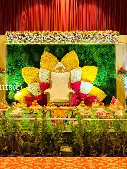 A wide view of a stage with our popular floral lotus backdrop. The setup is framed by lush greenery and includes a full display of offerings, creating a grand and festive look.