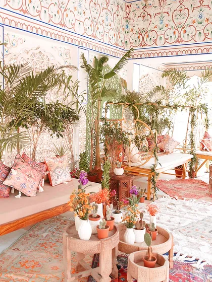 A wide view of a Mehendi lounge, featuring a mix of colorful rugs, plush seating, and abundant greenery. The goal is to create a space that is both beautiful and comfortable.