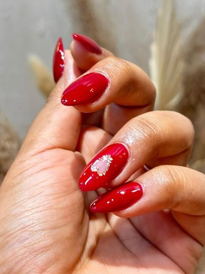 A close-up of our popular heart gem design. A classic, glossy red manicure is elevated with a sparkling, textured heart accent on the ring finger.