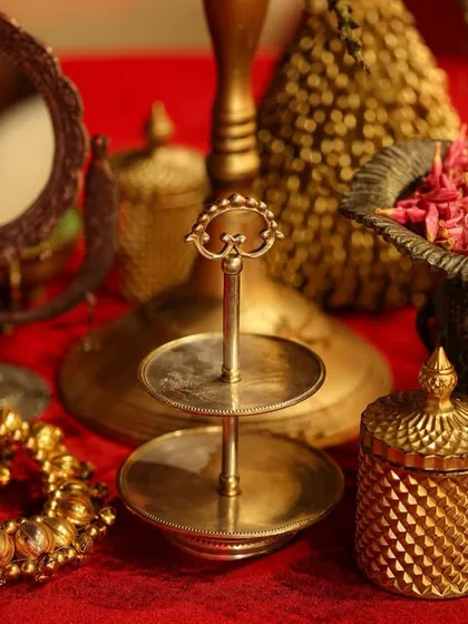 The details of a traditional tablescape, featuring antique-finish brass decor, a vintage-style mirror, and a bowl of fresh petals, all set on a rich red cloth.