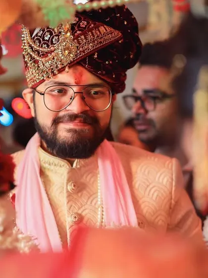 A candid shot of the groom during a wedding ritual. The focus is on his calm and happy expression as he participates in the ceremony.