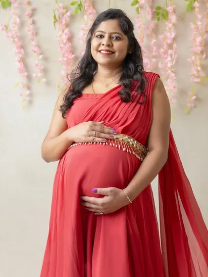 A close-up maternity portrait focusing on the joyful expression of the mom-to-be. The soft pink floral background adds a delicate and feminine touch.