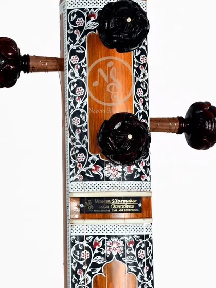 A close-up of the headstock of the floral tanpura. The dark, carved pegs contrast beautifully with the light-colored wood and intricate inlay.
