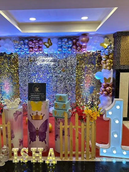 A glamorous take on the butterfly theme with a shimmering silver sequin backdrop. This first birthday setup includes a colorful balloon garland, a large light-up number "1", and butterfly-adorned plinths, creating a festive and sparkling photo corner.