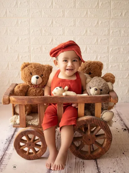 A happy boy in a red beret sits in a wooden cart filled with his teddy bear friends.