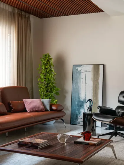 A detail of the informal living room, showcasing a curated collection of contemporary furniture and art. The timber-slatted ceiling and abstract painting add layers of texture and visual interest.