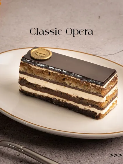 A perfect slice of my Classic Opera pastry. You can see the distinct layers of coffee-soaked almond sponge, rich ganache, and smooth buttercream, all topped with a glossy chocolate glaze.