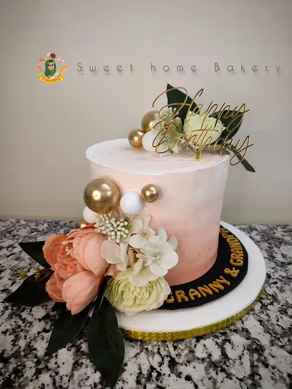 A lovely single-tier cake perfect for an intimate celebration or anniversary. The soft peach ombre buttercream is decorated with beautiful artificial flowers and gold sphere accents, creating a chic and modern look.