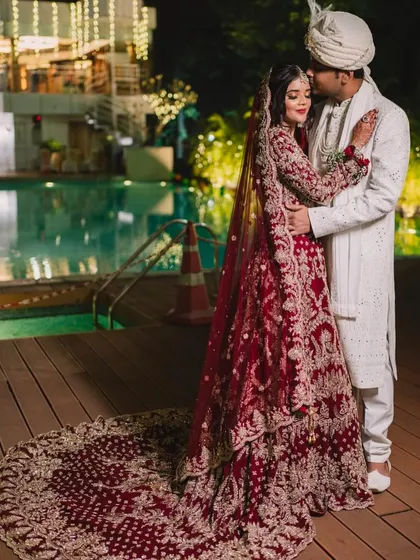 A breathtaking shot of the bride in her red gown with a long, dramatic trail, posing by the pool with her groom.