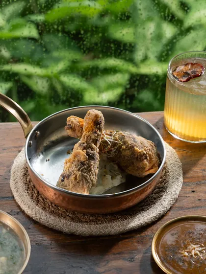 Crispy fried chicken legs served in a copper pan against a rainy backdrop. The steam rising from the chicken adds to the fresh-out-of-the-fryer feel.