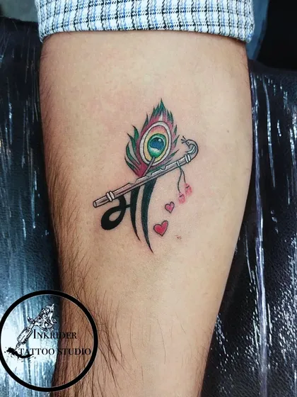 A creative design combining the word 'Maa' (Mother) with a peacock feather and a flute, symbolizing a mother's divine and beautiful nature.
