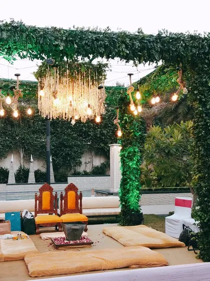 A unique mandap-style setup for a Haldi ceremony, constructed with pillars of lush greenery. The structure is accented with a crystal chandelier and string lights, creating a blend of natural and glamorous elements.