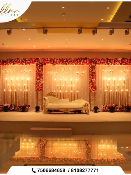 A beautiful reception stage with a floral border and a backdrop of warm string lights. The elegant chaise lounge adds a touch of classic sophistication.