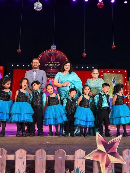 A full class of young students on stage in coordinated blue and black outfits, with sparkly vests for the boys and layered tulle skirts for the girls.